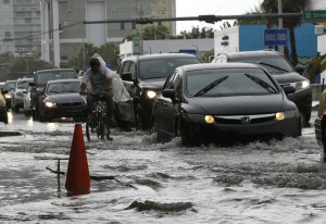 A cyclist and vehicles negotiate heavily flooded streets as rain falls, Tuesday, Sept. 23, 2014, in Miami Beach, Fla. 