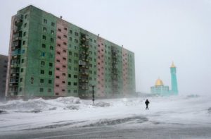 A man walks past a Soviet era housing block near the Nurd Kamal mosque in the arctic Russian city of Norilsk. Credit: Roger Bacon/REUTERS/Alamy